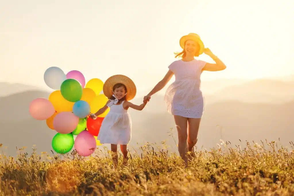 Mother and daughter walking outdoors with bright healthy smiles and colorful balloons
